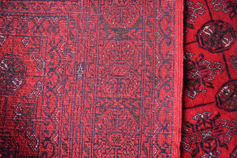 May include: Close-up of two red oriental rugs with intricate dark blue and brown patterns. The rugs have a textured surface and a detailed border design. The overall aesthetic is traditional and decorative.