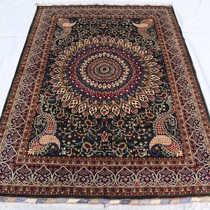 May include: A detailed, rectangular rug with a dark green base and elaborate floral and paisley designs in red, gold, and blue. The rug has a central medallion and decorative borders, with fringed edges.
