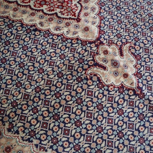 Puede incluir: Primer plano de una alfombra estampada con un esquema de color azul, rojo y crema. La alfombra tiene un dise&ntilde;o floral con detalles intrincados.