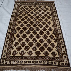 May include: A brown and cream patterned rug with a geometric design. The rug has a fringe border.
