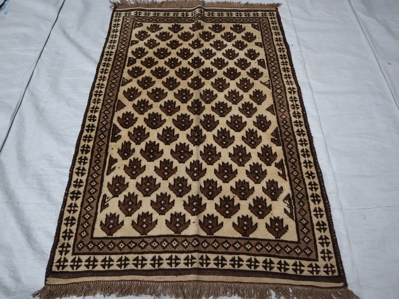 May include: A brown and cream patterned rug with a geometric design. The rug has a fringe border.