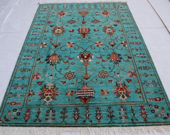 May include: A rectangular turquoise rug with an intricate floral pattern. The rug features a central design of stylized flowers and vases in shades of red, brown, and gold, framed by a detailed border. The rug has a fringe on the edges.