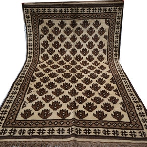 May include: A traditional rug with a cream background and a repeating pattern of brown stylized flowers. The rug has a brown border with a geometric design.