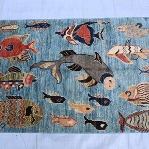 May include: A blue rug with a colorful fish design. The rug features a variety of fish in different colors and patterns, including red, orange, yellow, green, blue, and black. The rug is made of wool and has a soft, plush texture.