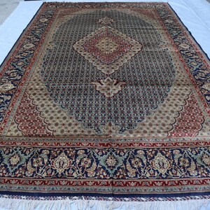 May include: A traditional Persian rug with a navy blue background and intricate floral patterns in shades of red, cream, and green. The rug has a central medallion and a border with a repeating design.