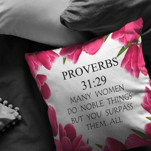 May include: White pillow with pink tulips printed on it. The pillow has black text that reads "Proverbs 31:29 Many women do noble things but you surpass them all".