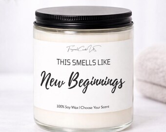 May include: A clear glass candle jar with a black metal lid, filled with off-white soy wax. The white label features the text "THIS SMELLS LIKE New Beginnings" in black, along with "100% Soy Wax | Choose Your Scent" at the bottom.