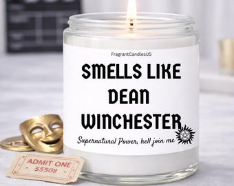 May include: A clear glass jar candle with a white wax fill and a lit wick. The label features the text FragrantCandlesUS, SMELLS LIKE DEAN WINCHESTER, and Supernatural Power, hell join me, along with a small circular pentagram symbol.