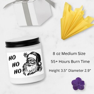 a medium-sized white jar with a Santa Claus illustration, a gift box, a yellow tissue paper, and a purple flower.