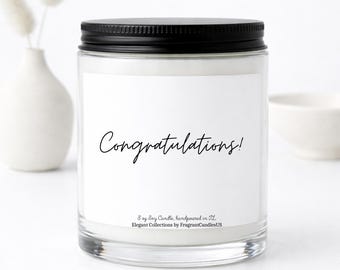 May include: A clear glass jar candle with a black lid and a white label featuring the black text Congratulations! and 8 oz Soy Candle, handpoured in FL, Elegant Collections by FragrantCandlesUS printed on the front of the container.