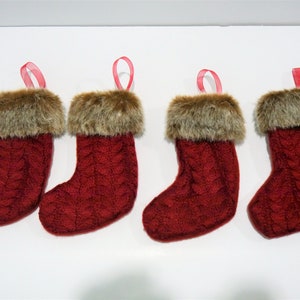 May include: Four red knitted Christmas stockings with faux fur trim and red ribbon loops.