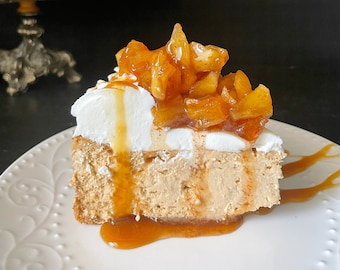 May include: A slice of cheesecake topped with a layer of whipped cream and caramelized apples. The cheesecake is drizzled with caramel sauce and served on a white plate.