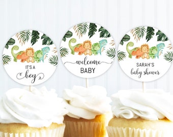Könnte beinhalten: Drei runde Cupcake-Topper mit Dinosaurier-Motiv. Die Topper zeigen einen grünen, orangefarbenen und gelben Dinosaurier mit grünen Blättern und dem Text "It's a boy", "Welcome Baby" und "Sarah's Baby Shower".