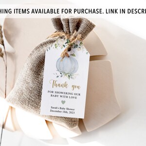 May include: A small burlap bag tied with twine, holding a gift tag. The tag features a watercolor illustration of a blue pumpkin with floral accents. Text on the tag reads "Thank you for showering our baby with love." The baby shower date is December 18th, 2023.