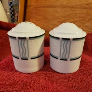 May include: Two white ceramic salt and pepper shakers with a black and blue geometric design. The shakers have a white background with a black and blue geometric design.