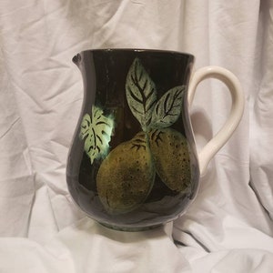 May include: A black ceramic pitcher with a white handle and a green and brown lemon design.