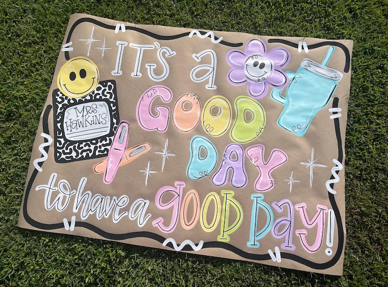 May include: A hand-painted sign on brown paper with the words "It's a Good Day to have a Good Day!" in colorful bubble letters. Includes a smiley face, flower, and drink illustration.