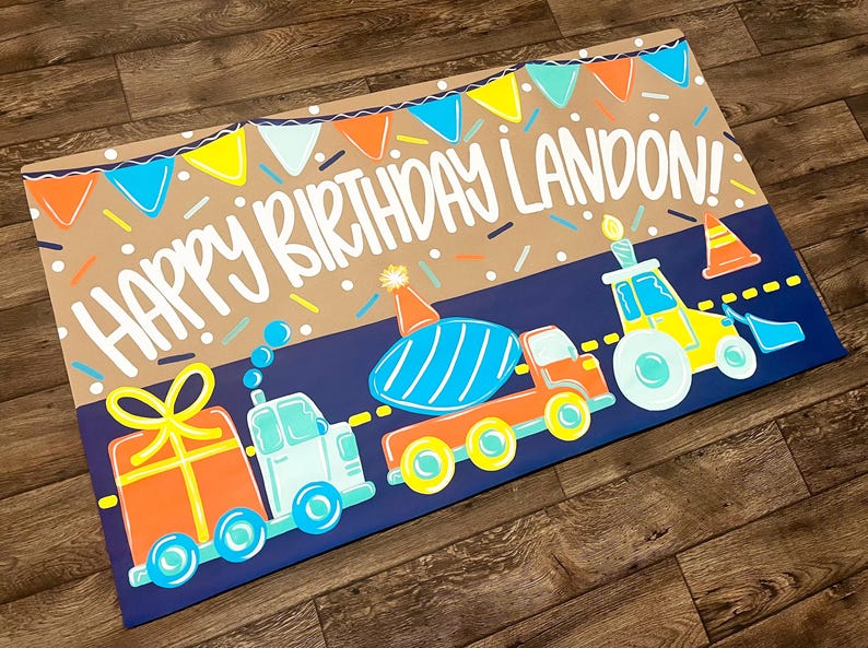 May include: A colorful birthday-themed illustration featuring the text "HAPPY BIRTHDAY LANDON!" above a row of cartoon vehicles. The design includes a gift, a truck, a cement mixer, and a tractor, all in bright colors, with confetti and bunting.