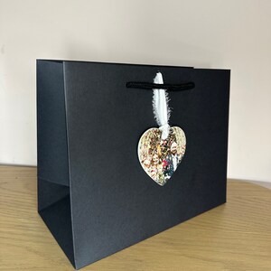 Peut inclure: Un sac cadeau noir avec une &eacute;tiquette photo en forme de c&oelig;ur attach&eacute;e. L'&eacute;tiquette photo pr&eacute;sente un groupe de personnes dans un cadre de mariage.