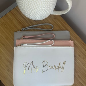 May include: Three zippered pouches in grey, pink and white with gold lettering that reads "Mrs. Beardall".