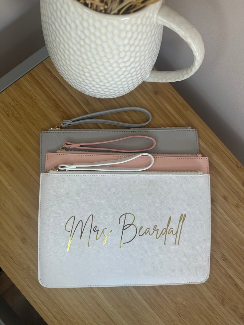 May include: Three zippered pouches in grey, pink and white with gold lettering that reads "Mrs. Beardall".