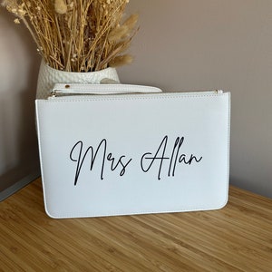 May include: White clutch bag with a zip closure. The bag has the text "Mrs Allan" printed in black cursive script.