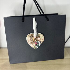 Peut inclure: Un sac cadeau noir avec une anse en cordon blanc. Un ornement en forme de c&oelig;ur avec une photo d'un groupe de mariage est attach&eacute; &agrave; l'anse.