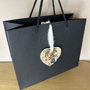 Peut inclure: Un sac cadeau noir avec une &eacute;tiquette en tissu blanc et un ornement photo en forme de c&oelig;ur. La photo montre un groupe de personnes.