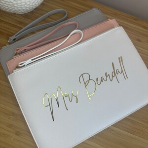 May include: Three white, pink and grey zippered pouches with gold handles. The largest pouch has the text "Mrs. Beardall" in gold script.