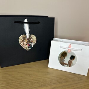 Peut inclure: Deux sacs cadeaux blancs avec des poign&eacute;es en ruban noir et blanc. Un sac a un ornement photo en forme de c&oelig;ur avec une photo de mariage. L'autre sac a un ornement photo rond avec une mari&eacute;e et une demoiselle d'honneur.