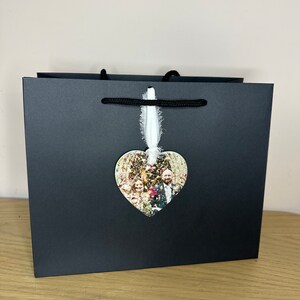 Peut inclure: Un sac cadeau noir avec un ruban blanc et un ornement photo en forme de c&oelig;ur repr&eacute;sentant un couple et des invit&eacute;s &agrave; un mariage.