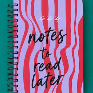 Può includere: Un taccuino con rilegatura a spirale caratterizzato da un motivo a righe verticali ondulate nei toni del viola chiaro e del rosso brillante. La copertina presenta tre stelle bianche disegnate a mano in alto e il testo nero "notes to read later".