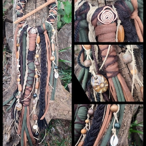 Op de afbeelding: Een handgemaakte dromenvanger met een houten hoepel gewikkeld in groene, bruine en crèmekleurige stof. Het heeft hangende strengen stof, kralen, schelpen en houten accenten, wat een bohemien esthetiek creëert.