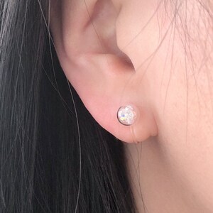 May include: A close-up of a person's ear with a clear crystal earring. The earring has a small, round shape and is set in a silver setting.