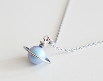 May include: A silver chain necklace with a blue and purple iridescent orb pendant. The orb is surrounded by a silver ring, and the pendant is attached to the chain with a silver anchor.