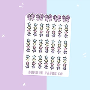 May include: A sheet of colorful star stickers with a pink, yellow, and blue color scheme. The sheet has a scalloped edge and features four bows at the top. The text "DEMURE PAPER CO" is printed at the bottom of the sheet.