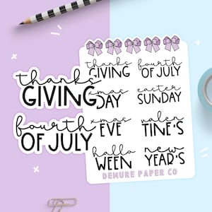 May include: A sheet of stickers with various holiday and seasonal phrases, including "thanksgiving", "fourth of july", "christmas", "easter", "halloween", and "new year's". The stickers are white with black text and feature a purple bow design.