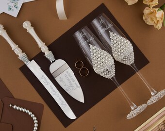 May include: A wedding cake serving set with two silver cake knives and two champagne flutes. The knives have the words "Love Never Fails" and "Forever and Ever Mr. & Mrs. Ferrari" engraved on them. The flutes are decorated with white pearls and have the words "Mr. Ferrari" and "Mrs. Ferrari" engraved on them.