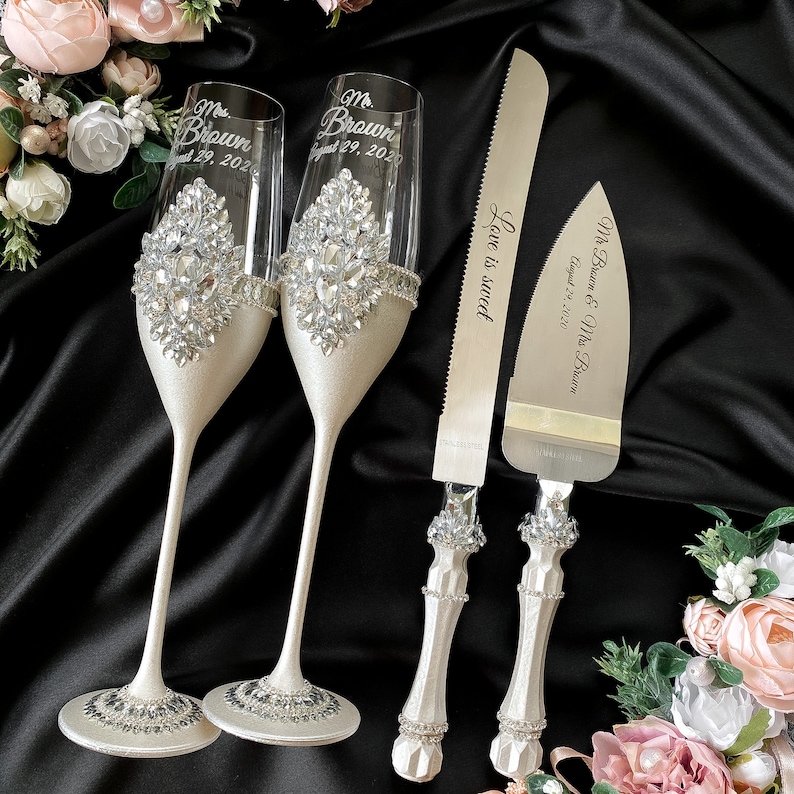 Puede incluir: Un juego de corte de pastel de bodas con dos copas de champ&aacute;n y un cuchillo. Las copas est&aacute;n decoradas con diamantes de imitaci&oacute;n y tienen el texto "Mr. Brown August 29, 2020" y "Mrs. Brown August 29, 2020" grabado en ellas. El cuchillo tiene el texto "Mr. Brown & Mrs. Brown August 29, 2020" y "Love is sweet" grabado en &eacute;l.