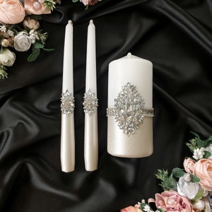 Puede incluir: Tres velas de boda de marfil con adornos de pedrer&iacute;a plateada. La vela central es m&aacute;s grande que las dos velas laterales.