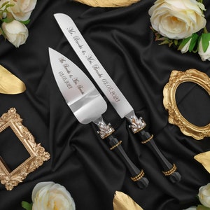 May include: A set of two silver wedding cake knives with black handles and gold accents. The knives are engraved with the text "Mr. Brooks & Mrs. Brooks 03.05.2023".