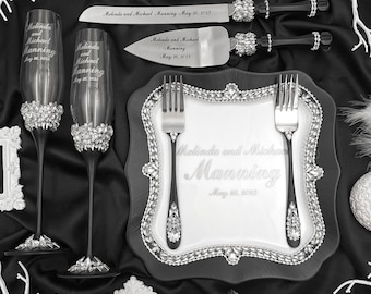 May include: Elegant wedding table setting with champagne flutes, cake server, and plate. The items are adorned with rhinestones and the names "Melinda and Michael Manning May 26, 2023" are engraved on the items. The setting is on a black satin cloth.