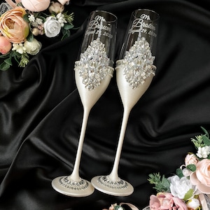 Puede incluir: Dos copas de champ&aacute;n con un acabado blanco y brillante. Las copas est&aacute;n decoradas con una banda de pedrer&iacute;a y tienen las palabras "Mr. Brown August 29, 2020" y "Mrs. Brown August 29, 2020" grabadas en ellas.