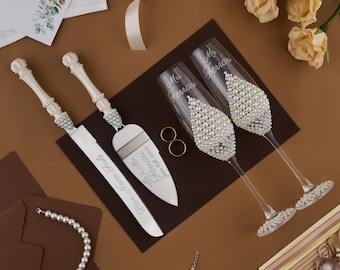 May include: A wedding cake cutting set with a white handle and silver blade, two champagne flutes with pearl embellishments, and the text "Love Never Fails" and "Mr. & Mrs. Ferrari" engraved on the set.