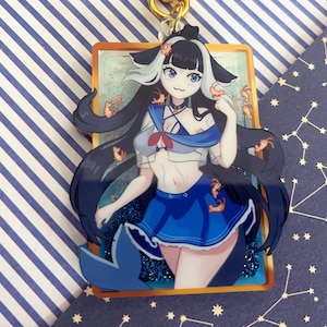 以下が含まれることがあります： セーラー服を着たキャラクターが描かれた、カラフルなアニメスタイルのキーホルダー。黒髪と青い目。キャラクターは、小さなオレンジ色のカニのイラストと青いキラキラしたベースの背景に設定されています。キーホルダーには金色の金属リングが付いています。
