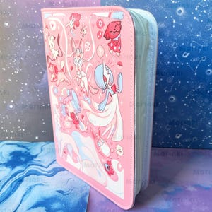 Peut inclure: Un classeur rectangulaire rose à fermeture éclair orné d'un imprimé graphique coloré représentant diverses créatures de dessin animé stylisées. La couverture présente plusieurs personnages dans des tons rose, blanc et bleu.