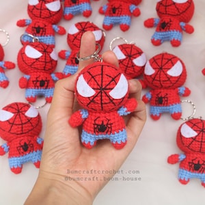 Può includere: Portachiavi di Spider-Man all'uncinetto rossi e blu. Ogni portachiavi presenta una testa rossa con dettagli occhi bianchi e un emblema di ragno nero. Il corpo è rosso con pantaloncini e braccia blu. È attaccato un portachiavi argentato.