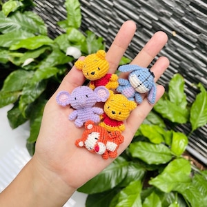 May include: A collection of small, crocheted character figures in various colors. The figures include a yellow bear with a red shirt, a purple elephant, a blue donkey, and an orange tiger. The figures are handmade and appear to be part of a children's theme.