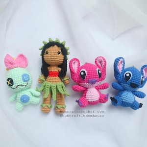 May include: Four crocheted stuffed toys: a blue Stitch, a pink Angel, a green Stitch with a pink bow, and a brown-skinned girl with black hair wearing a green grass skirt and a red top.