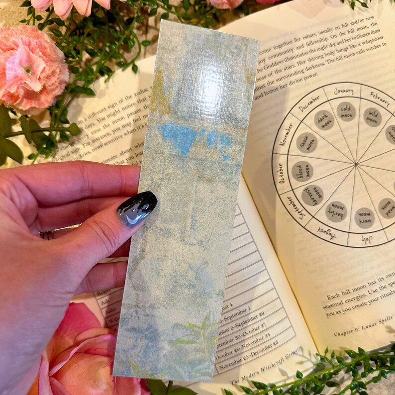 May include: A vintage-style bookmark with a watercolor design of a blue and green landscape. The bookmark is made of paper and has a slightly textured surface.